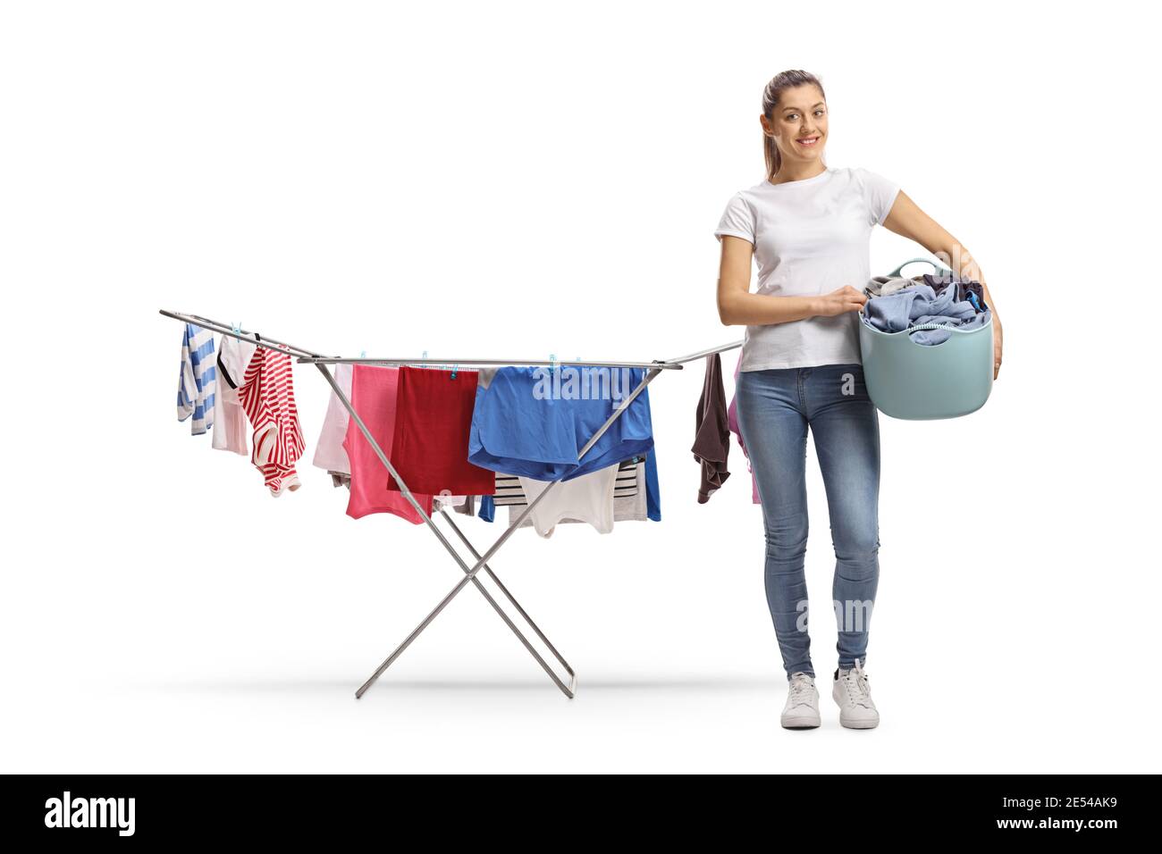 Ritratto a lunghezza intera di una giovane femmina casual che tiene un cestino di lavanderia e in piedi accanto ad una linea di abbigliamento rack isolato su sfondo bianco Foto Stock
