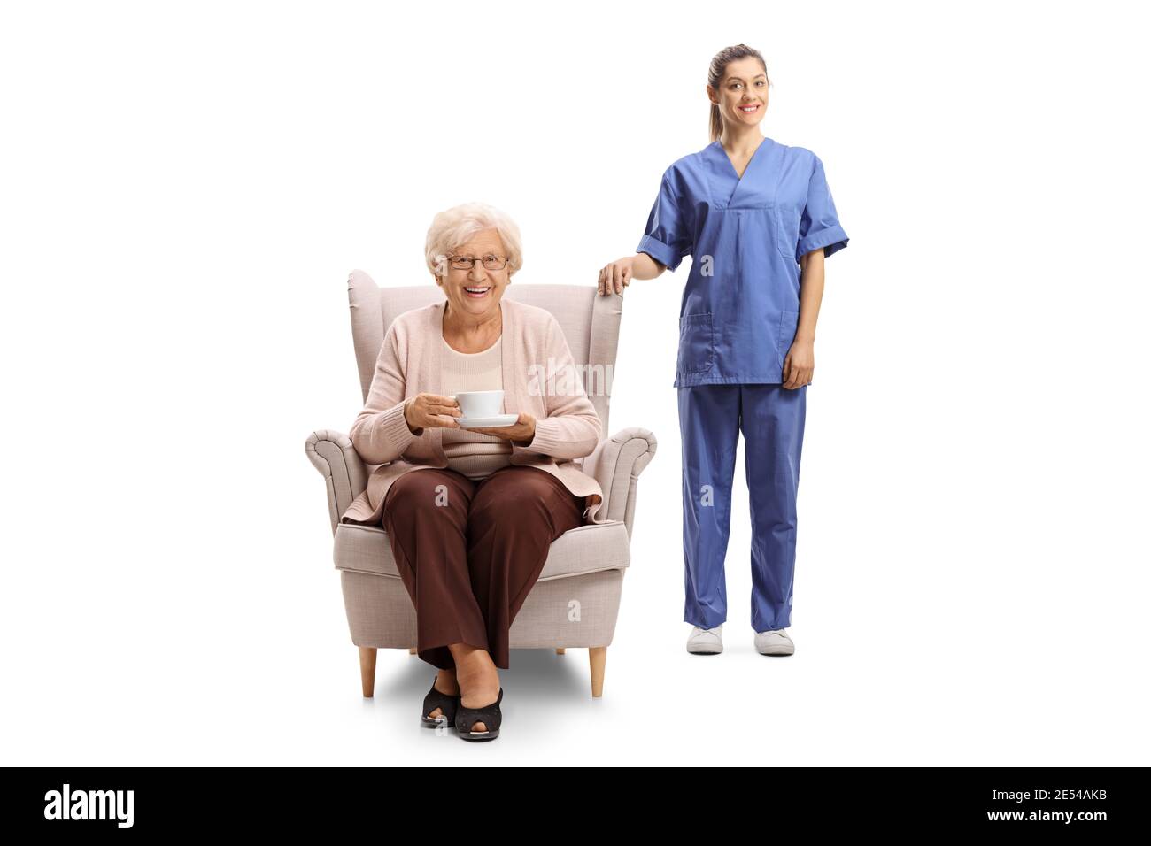 Infermiera femminile in piedi accanto ad una donna anziana in un poltrona con una tazza di tè isolato su sfondo bianco Foto Stock