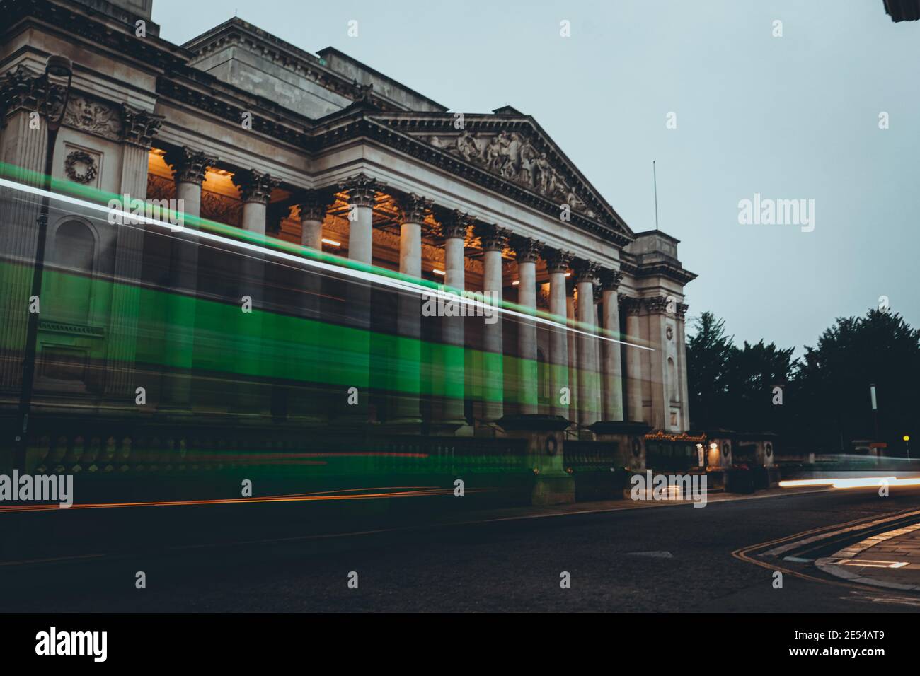 Lunga esposizione di un autobus verde che passa di fronte il museo dell'architettura nella città di cambridge Foto Stock