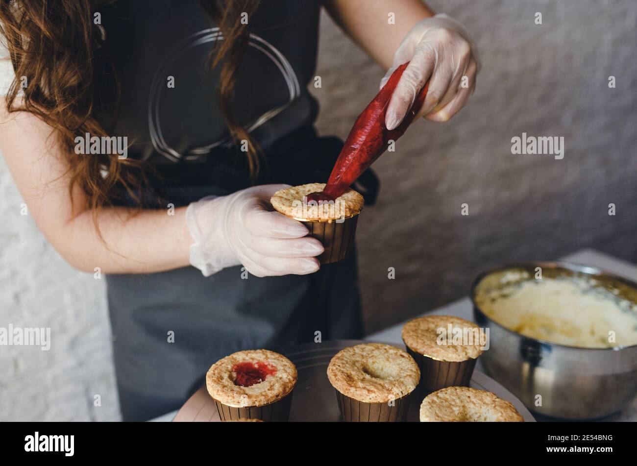 la ragazza cuoce cupcakes a casa. Mani di uno chef con un sacchetto di pasticceria, spremendo la crema sulle cupcakes Foto Stock