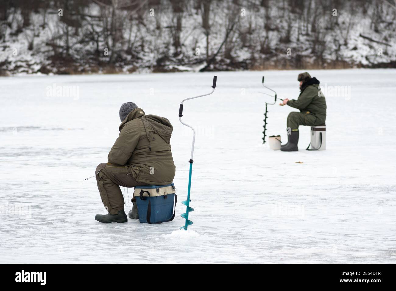 Pescatori che pescano su un lago ghiacciato in inverno con canna da pesca, trivella e attrezzature per la pesca Foto Stock