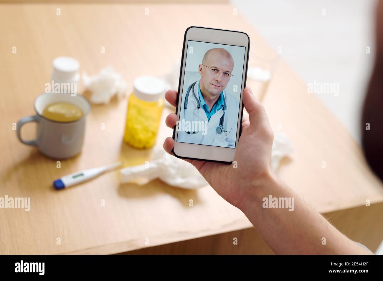 Medico di sesso maschile maturo sullo schermo dello smartphone guardando il paziente e. dare consigli medici al giovane malato descrivendo i suoi sintomi Foto Stock