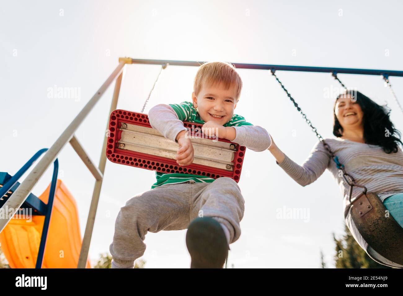 Ragazzo allegro che si diverte a oscillare con la mamma. Vista ad angolo basso di un bambino felice che oscilla con la madre in un parco giochi. Foto Stock