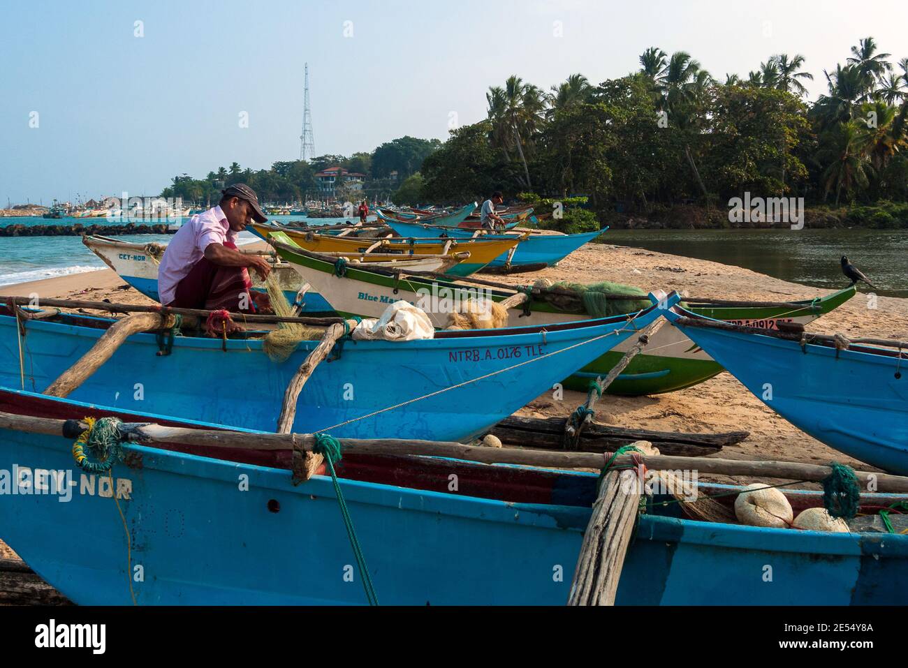Tangalle, Sri Lanka: I pescatori riparano le reti sulle barche che si trovano sulla spiaggia della città Foto Stock