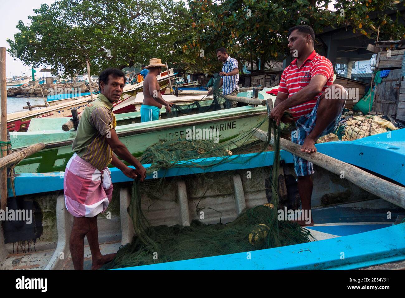 Tangalle, Sri Lanka: I pescatori riparano le reti sulle barche sulla spiaggia della città Foto Stock