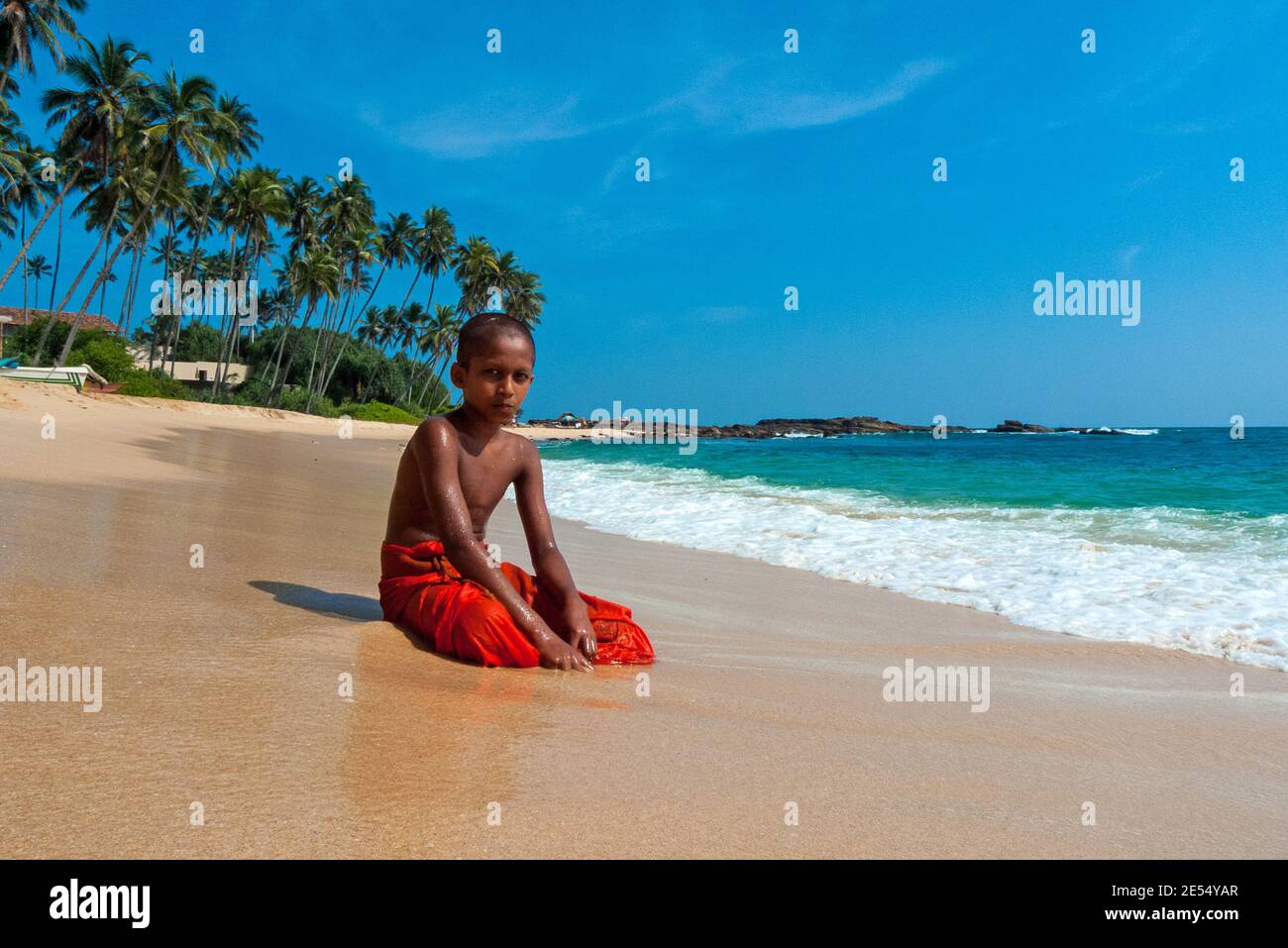 Tangalle, Sri Lanka: Un bambino buddista novizio seduto in riva al mare Foto Stock