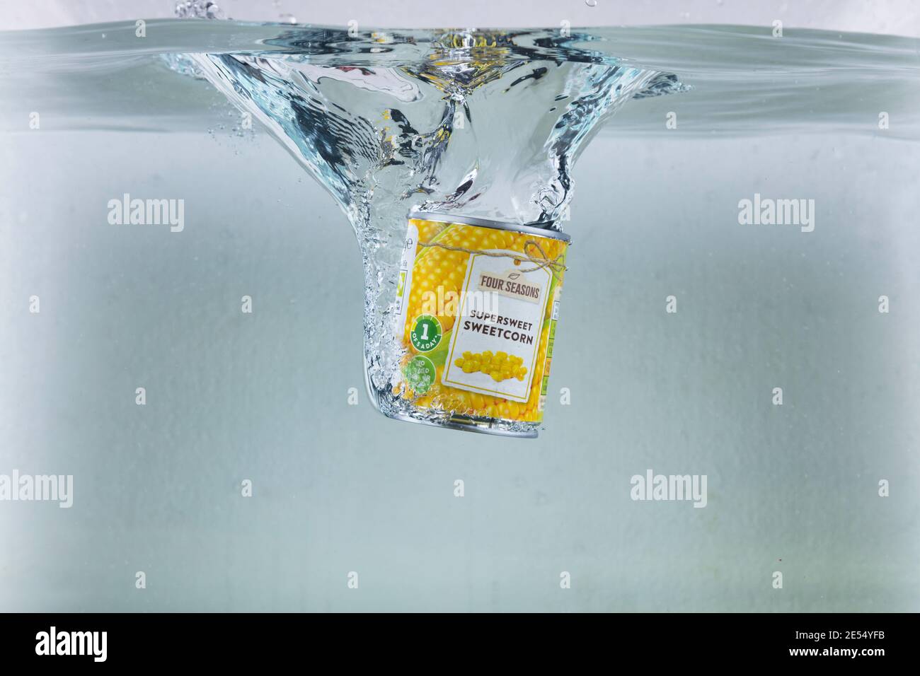 Colpo ad alta velocità di una latta di granturco dolce che cade in acqua. Ultra alta velocità di 1/5000esimo di secondo. Foto Stock