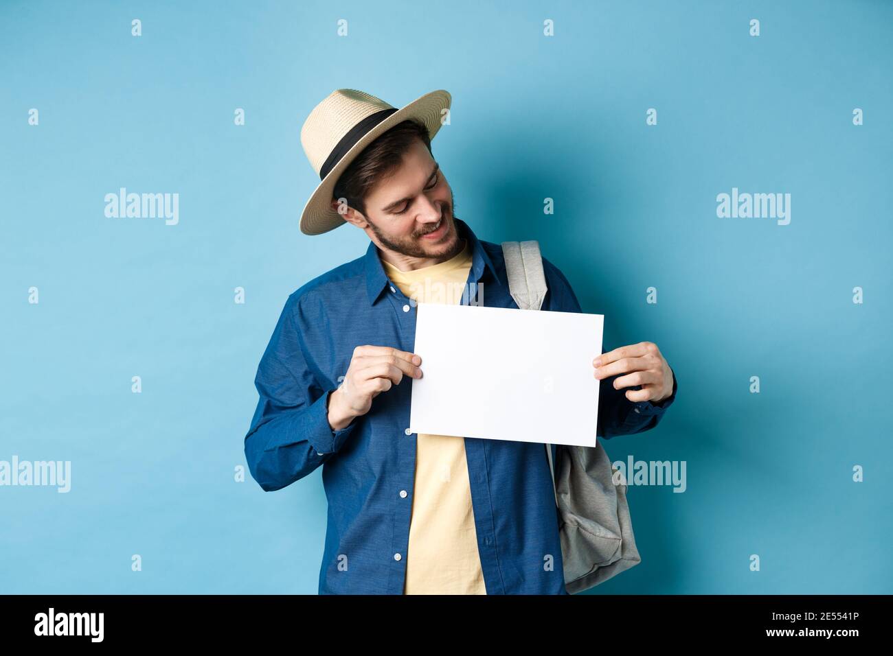 Turista felice in cappello di paglia sorridente e guardando un pezzo di  carta per il vostro logo, in piedi su sfondo blu Foto stock - Alamy