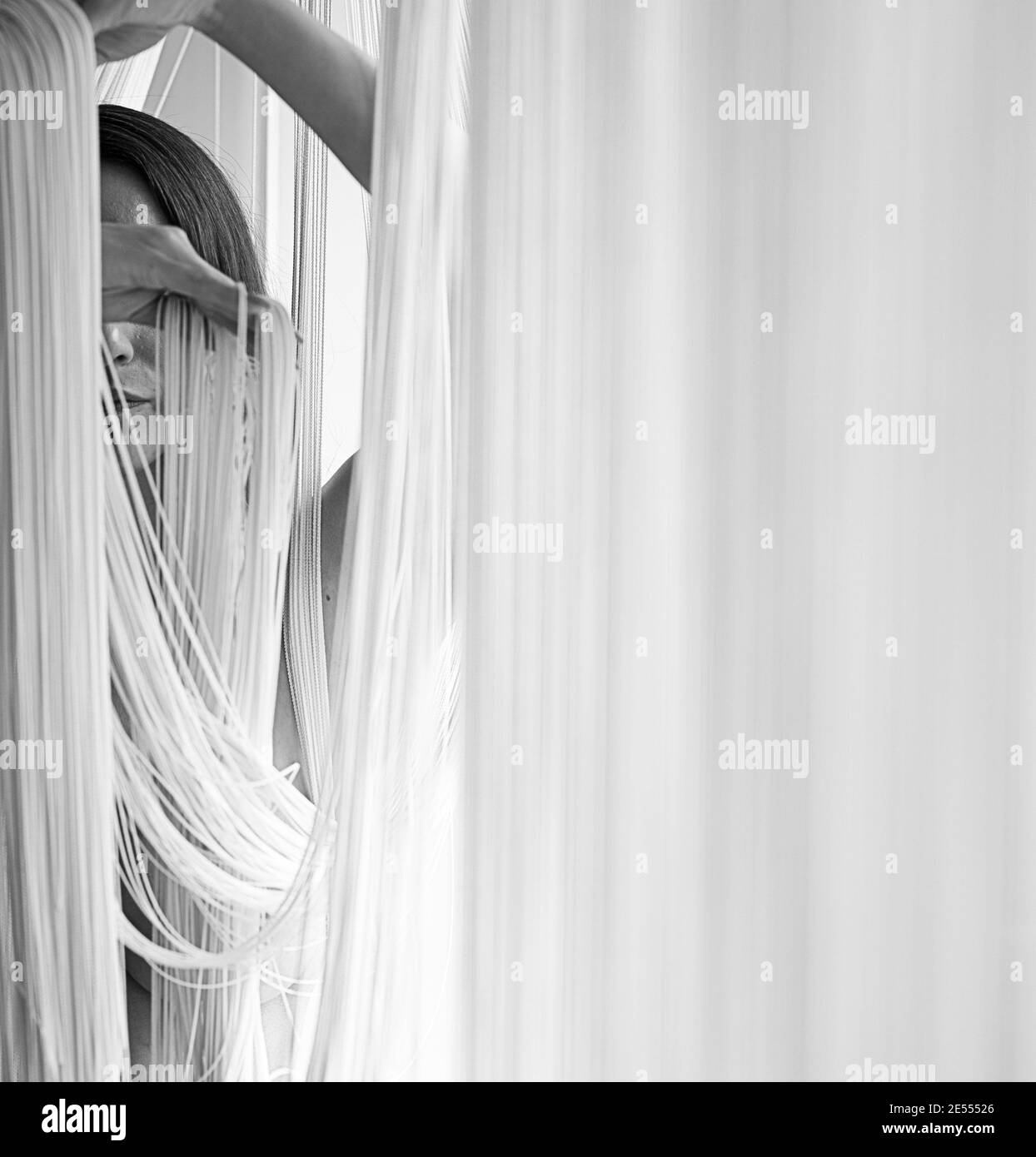 Ritratto di una giovane donna attraente con spalle scoperte che tira decorativamente i fili di una tenda a corda con le mani in bianco e nero. Imag Foto Stock