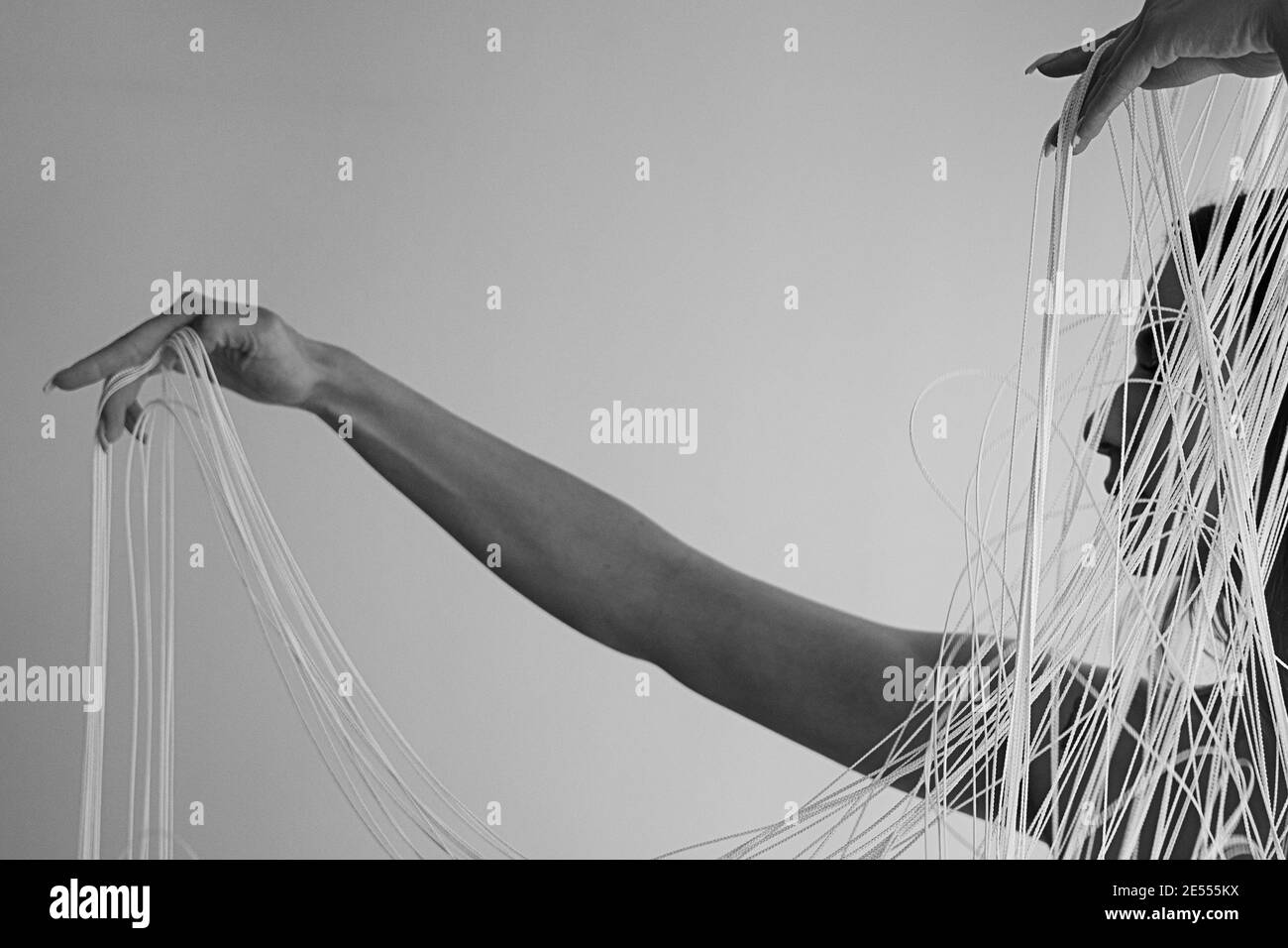 Bianco e nero immagine del profilo di un giovane donna attraente con spalle scoperte che tira decorativamente i fili bianchi di una tenda a corda w Foto Stock