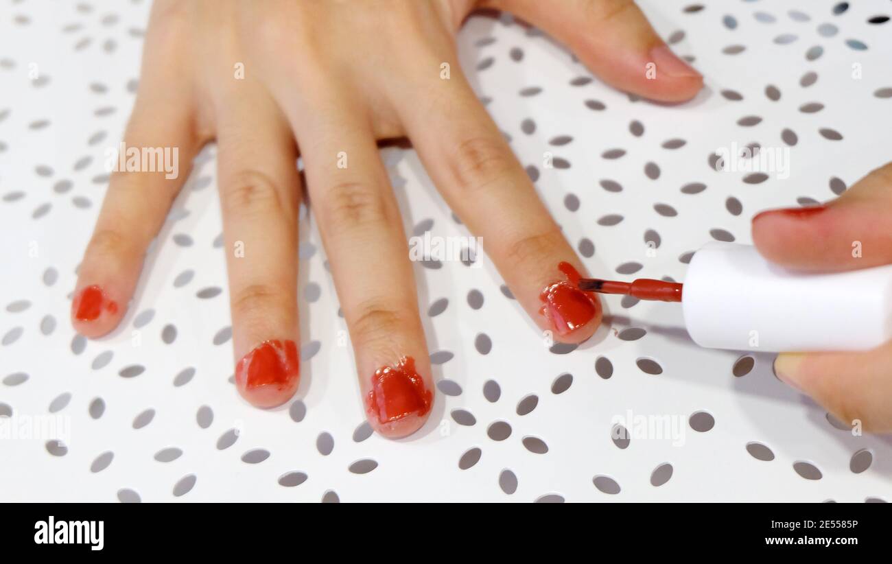 Dita con smalto rosso per unghie verniciate in modo disordinato. Foto Stock