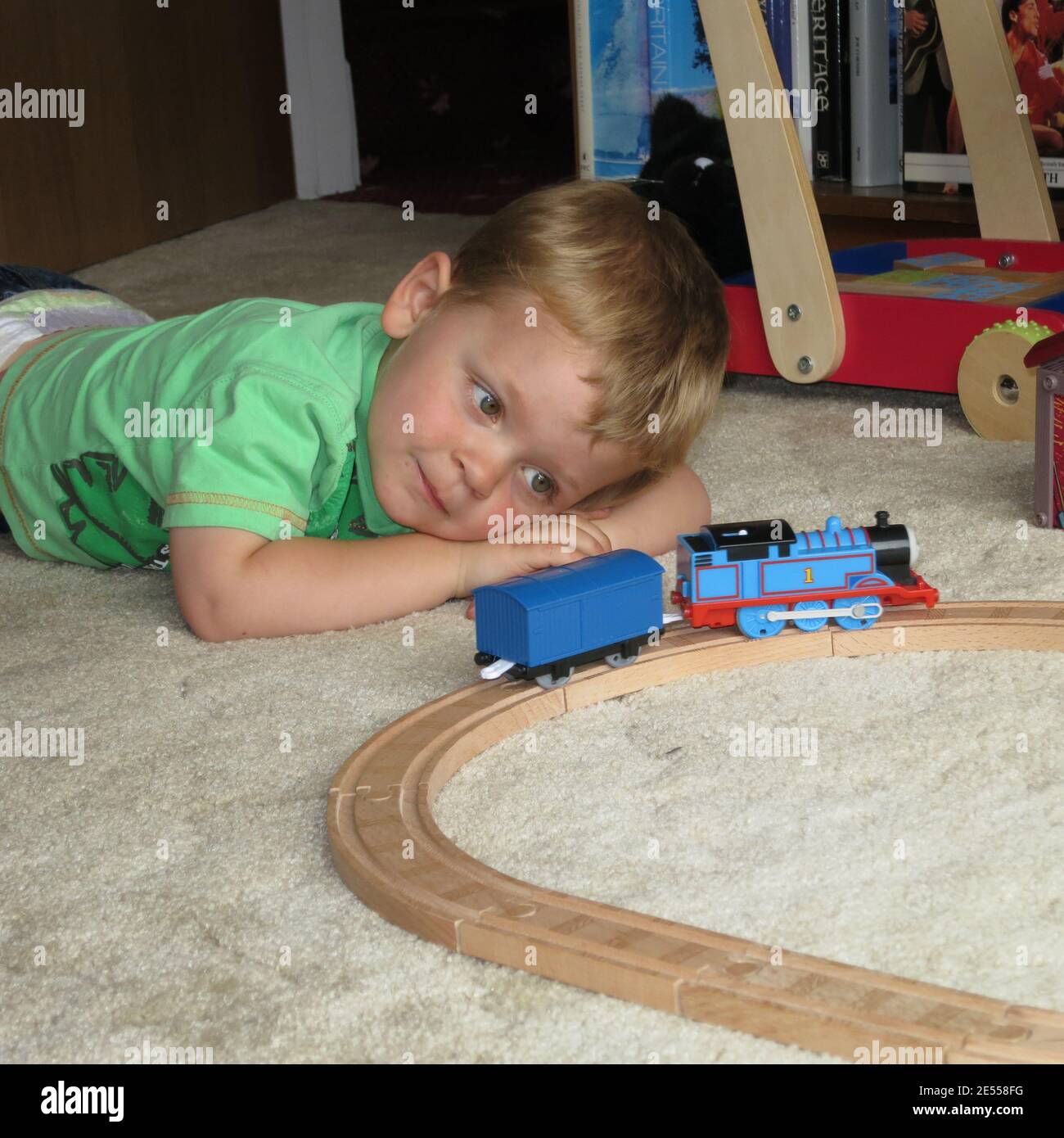 Ragazzo giovane che gioca con treno di legno posto sul pavimento Foto Stock
