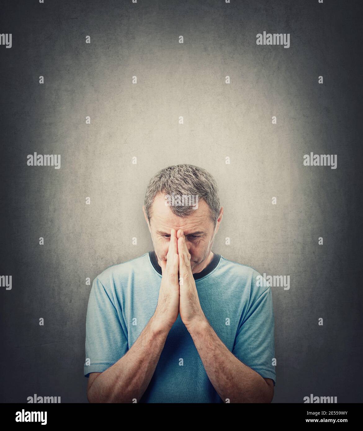 Uomo depresso di mezza età che prega su sfondo grigio parete con spazio copia sopra la testa. Uomo anziano disperato guardando verso il basso, tiene insieme le mani come pr Foto Stock