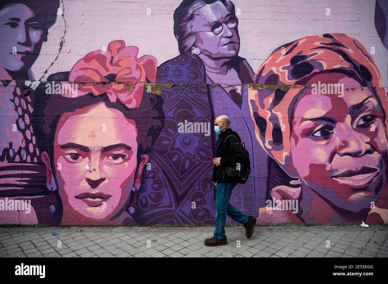 Madrid, Spagna. 26 gennaio 2021. Un uomo che indossa una maschera per proteggere contro la diffusione del coronavirus (COVID-19) cammina da un murale femminista chiamato 'Union Makes force' con le facce dipinte del pittore messicano Frida Kahlo e della musicista americana Nina Simone tra gli altri. Il partito di estrema destra VOX ha proposto la rimozione del murale che alla fine non sarà rimosso dal momento che Ciudadanos Party ha cambiato il suo voto. Nel murale appaiono i volti di 15 donne che fanno parte della storia per la loro lotta a favore dell'uguaglianza. Credit: Marcos del Mazo/Alamy Live News Foto Stock