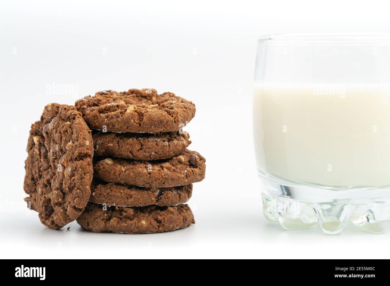 Pila di biscotti dolci al cioccolato fatti in casa con un bicchiere di latte su sfondo bianco. Foto Stock