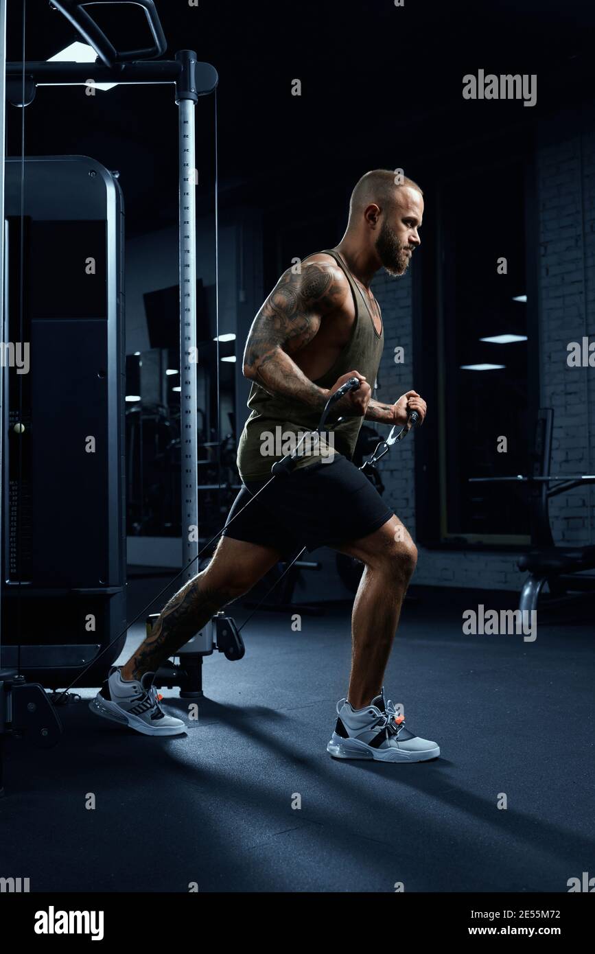 Ritratto di bodybuilder con cuscinetti muscolari che fa esercizio di  crossover a basso cavo. Vista laterale dell'uomo con petto perfetto per  l'allenamento del corpo in palestra in atmosfera buia Foto stock -