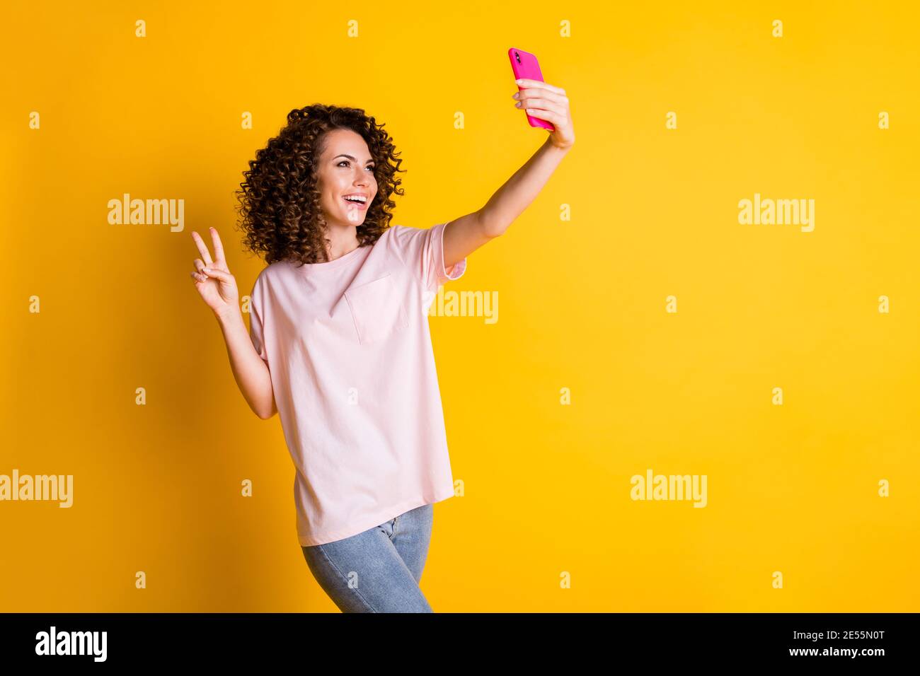 Ritratto fotografico di ragazza riccia che prende selfie dimostrando gesto v-segno pace isolato su sfondo giallo luminoso con copyspace. Foto Stock