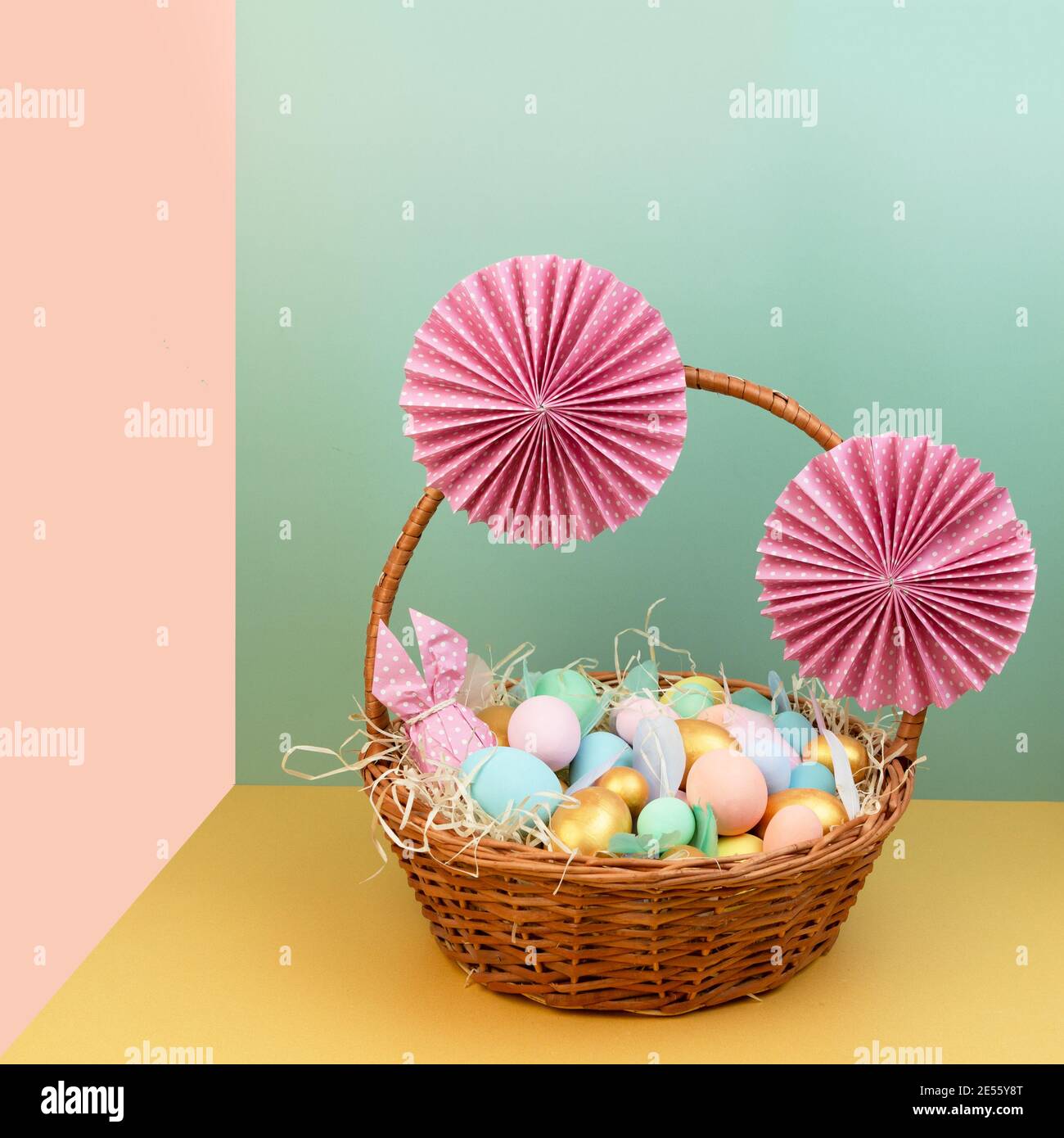 Cesto di vimini con colorate uova di Pasqua in colori pastello e decorato con fiori di carta. Foto Stock