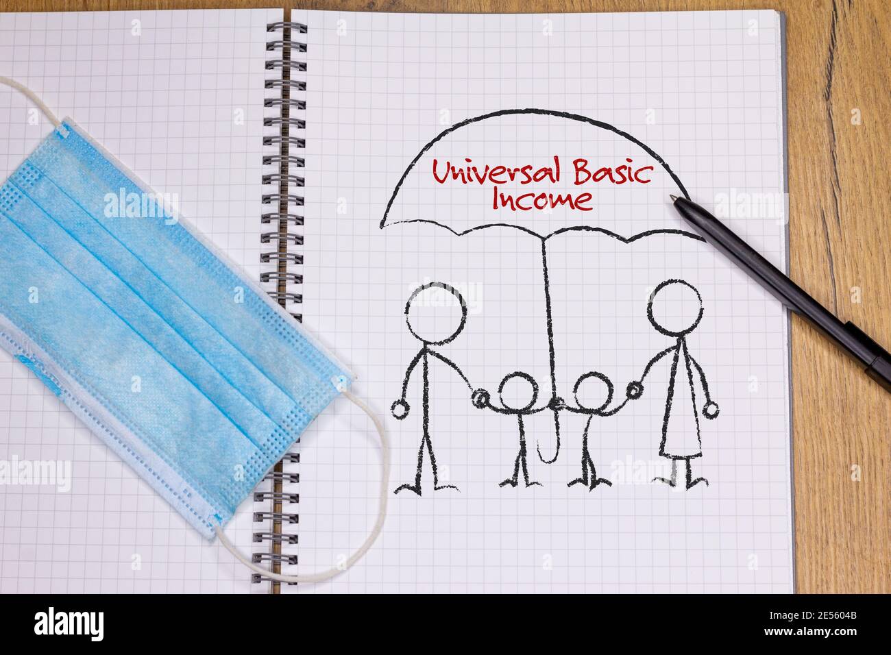 Disegnando sulla nota di famiglia sotto l'ombrello protettivo del reddito di base universale, accanto alla maschera facciale, covid post pandemico 19 reddito incondizionato Foto Stock