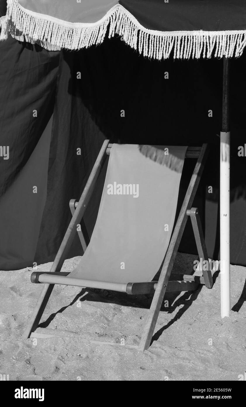 Spiaggia chaise lounge in legno e ombrellone con frangia. Trouville-sur-Mer (Normandia, Francia). Messa a fuoco selezionata sul margine. Foto obsolata. Bianco e nero. Foto Stock