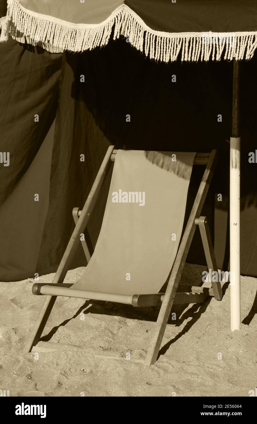 Spiaggia chaise lounge in legno e ombrellone con frangia. Trouville-sur-Mer (Normandia, Francia). Messa a fuoco selezionata sul margine. Foto obsolata. Seppia. Foto Stock