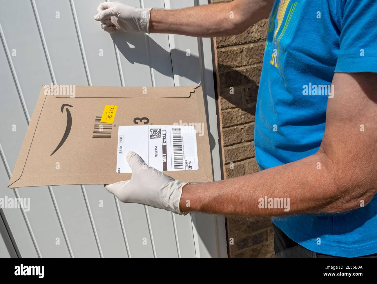 L'addetto alla consegna bussa alla porta di una casa per consegnare un pacco Amazon. Foto Stock