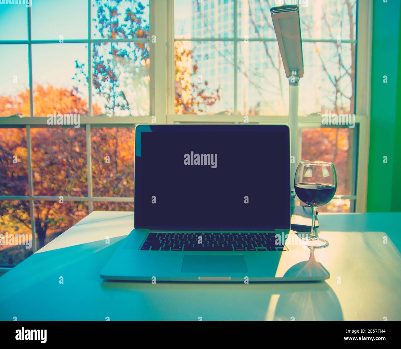 Primo piano di computer portatile con bicchiere di vino e alberi caduta sullo sfondo. Foto Stock