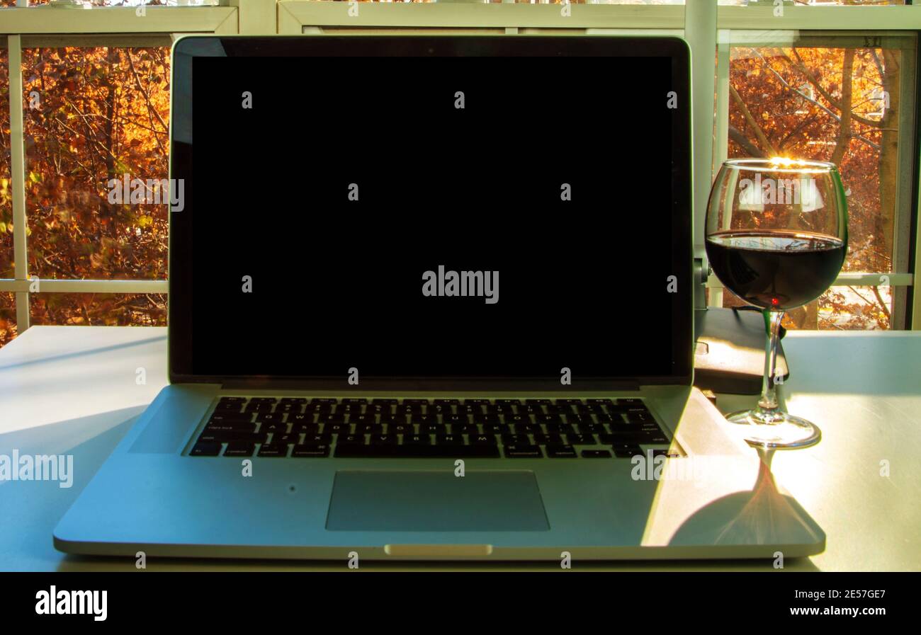 Primo piano di computer portatile con bicchiere di vino e alberi caduta sullo sfondo. Foto Stock