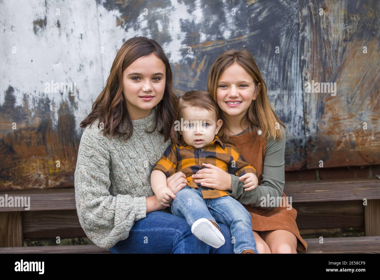 Due sorelle e un piccolo fratello seduto sui gradini esterno per un ritratto Foto Stock
