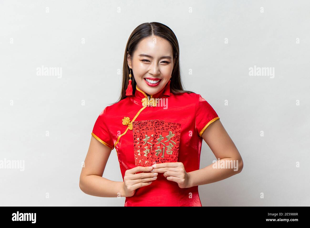 Sorridente donna asiatica felice in costume orientale tradizionale che tiene buste rosse o Ang Pao in grigio chiaro sfondo per i concetti di nuovo anno cinese, te Foto Stock