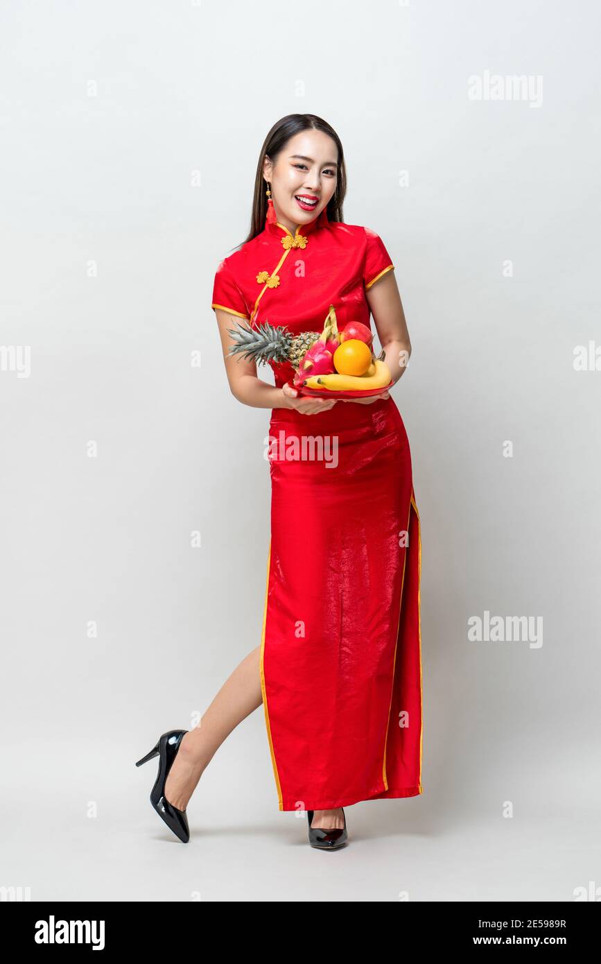 Giovane donna asiatica in abito traditinal rosso cheongsam tenendo fortunato Frutta per il nuovo anno cinese in uno studio isolato grigio chiaro sfondo Foto Stock