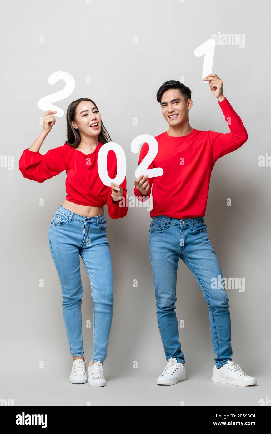 Ritratto a lunghezza intera di allegra coppia asiatica in abbigliamento casual sorridendo e mostrando il numero 2021 per il concetto di nuovo anno su isolato grigio chiaro studio retro Foto Stock