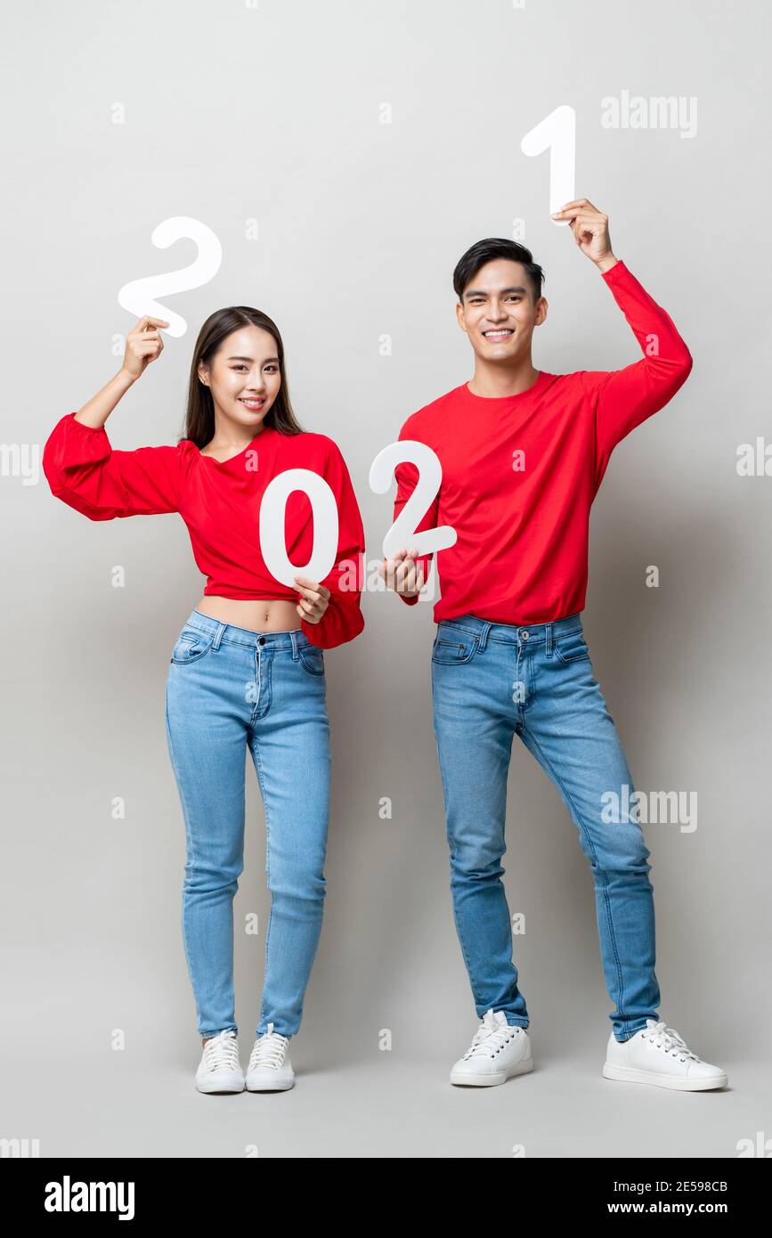 Ritratto a lunghezza intera di felice coppia asiatica in abbigliamento casual sorridendo e mostrando il numero 2021 per il concetto di nuovo anno su isolato grigio chiaro studio backgro Foto Stock