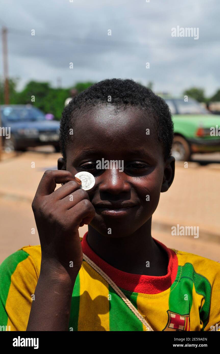 Un ragazzo Burkinabe che tiene una moneta da 100 franchi dell'Africa occidentale. Foto Stock