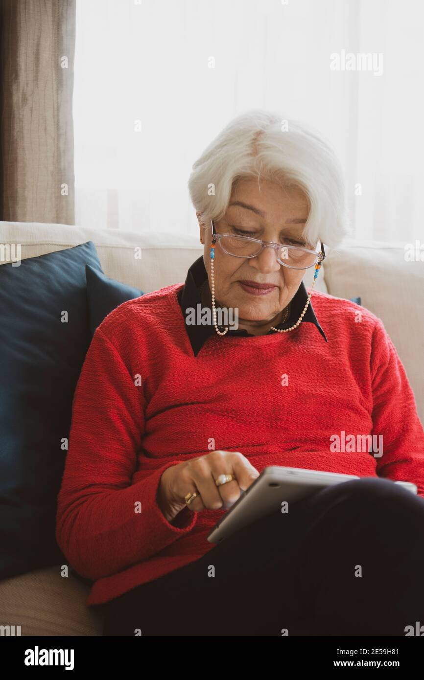 donna in pullover rosso seduta sul divano bianco, ha avuto cattive notizie sul telefono Foto Stock