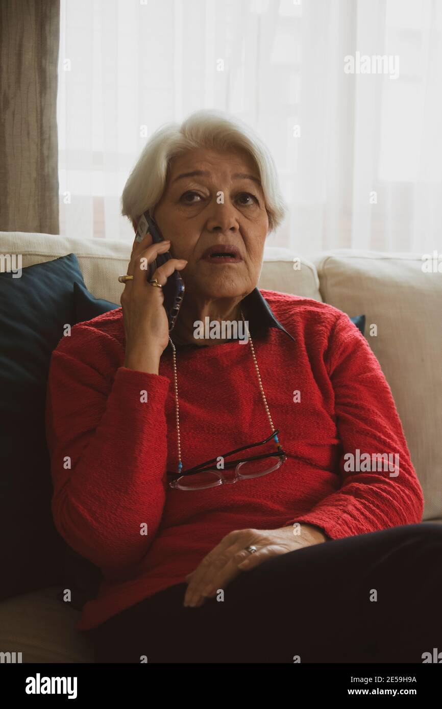 donna in pullover rosso seduta sul divano bianco, ha avuto cattive notizie sul telefono Foto Stock