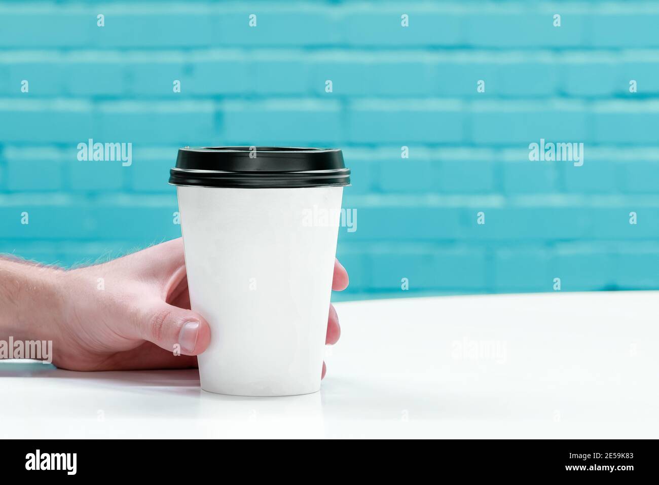 Primo piano della mano che tiene il caffè da togliere. Sfondo a parete in mattoni con spazio per la copia del testo Foto Stock