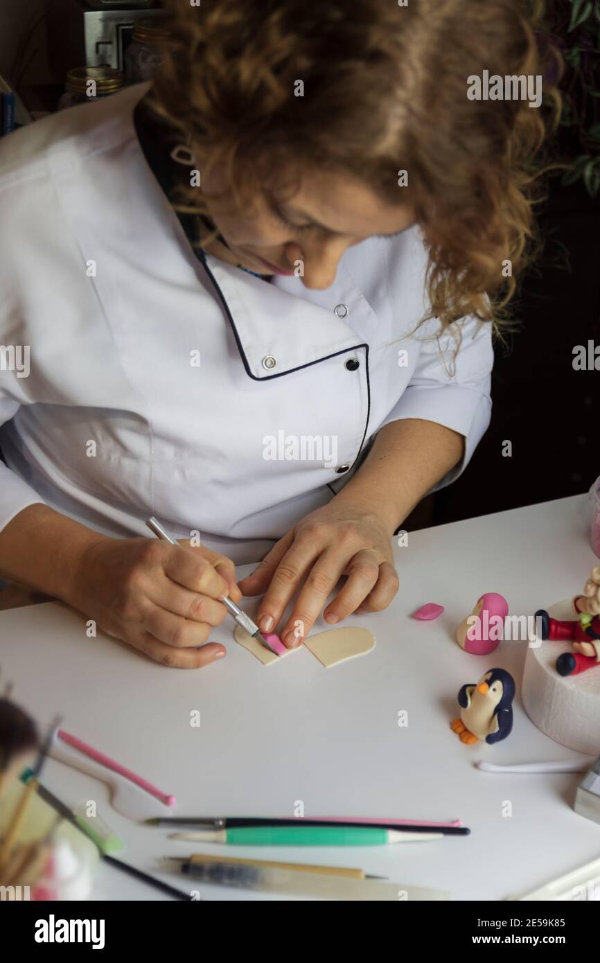 Processo di decorazione della torta. Baker usa gli strumenti per scolpire i modelli fondenti: Arte commestibile, disegno della torta, decorazione della torta. Messa a fuoco selettiva degli attrezzi anteriori e della mano Foto Stock