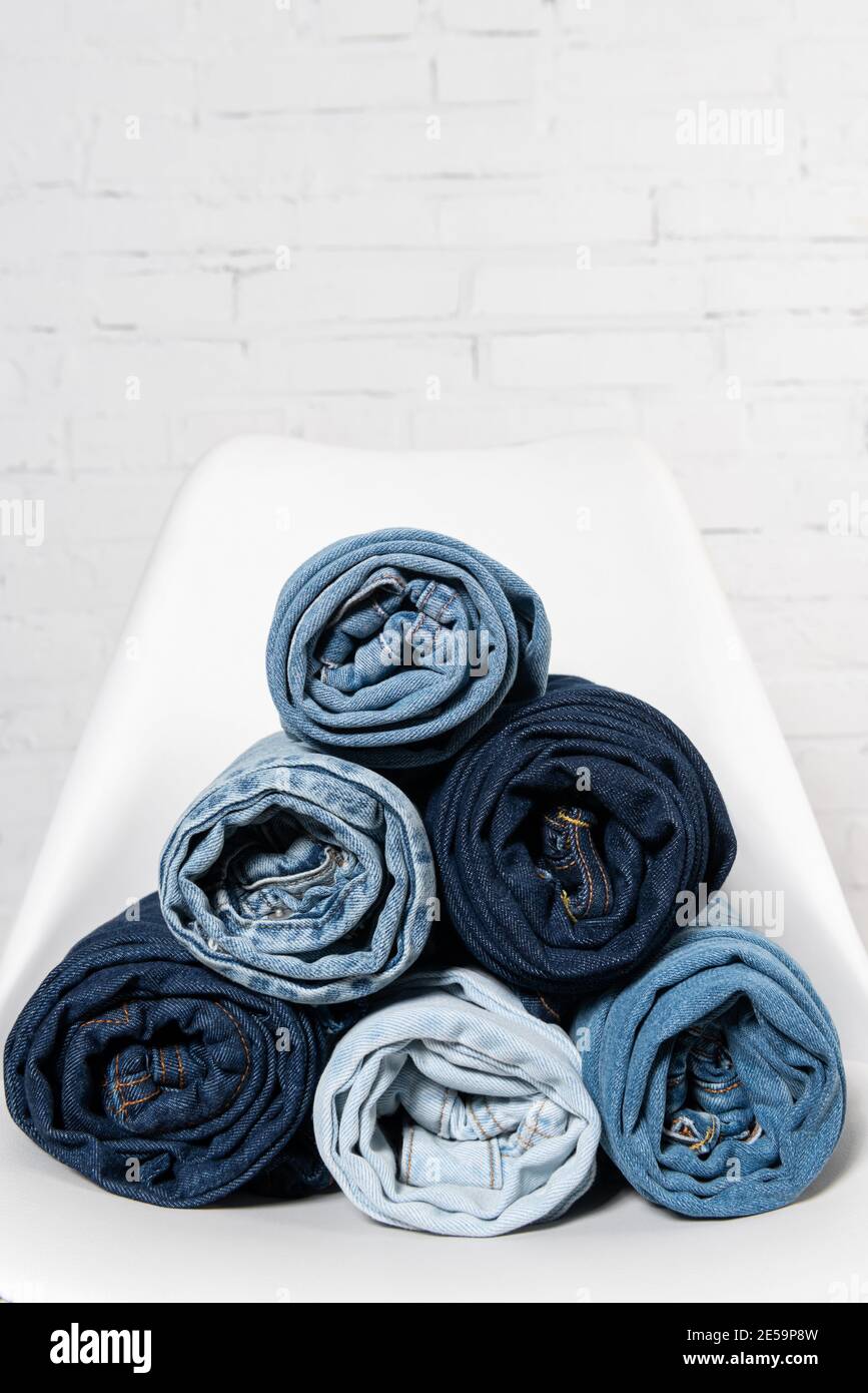 vista ravvicinata dei jeans arrotolati sulla sedia bianca vicino muro di mattoni Foto Stock