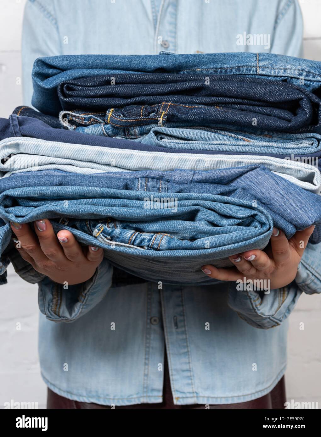 vista parziale di una donna che tiene vestiti in denim impilati Foto Stock