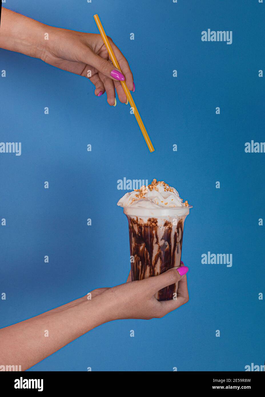 La mano della donna tiene un bicchiere di cocktail al cioccolato al latte con caffè con panna montata su sfondo blu. La mano di una donna tiene una cannuccia da cocktail Foto Stock