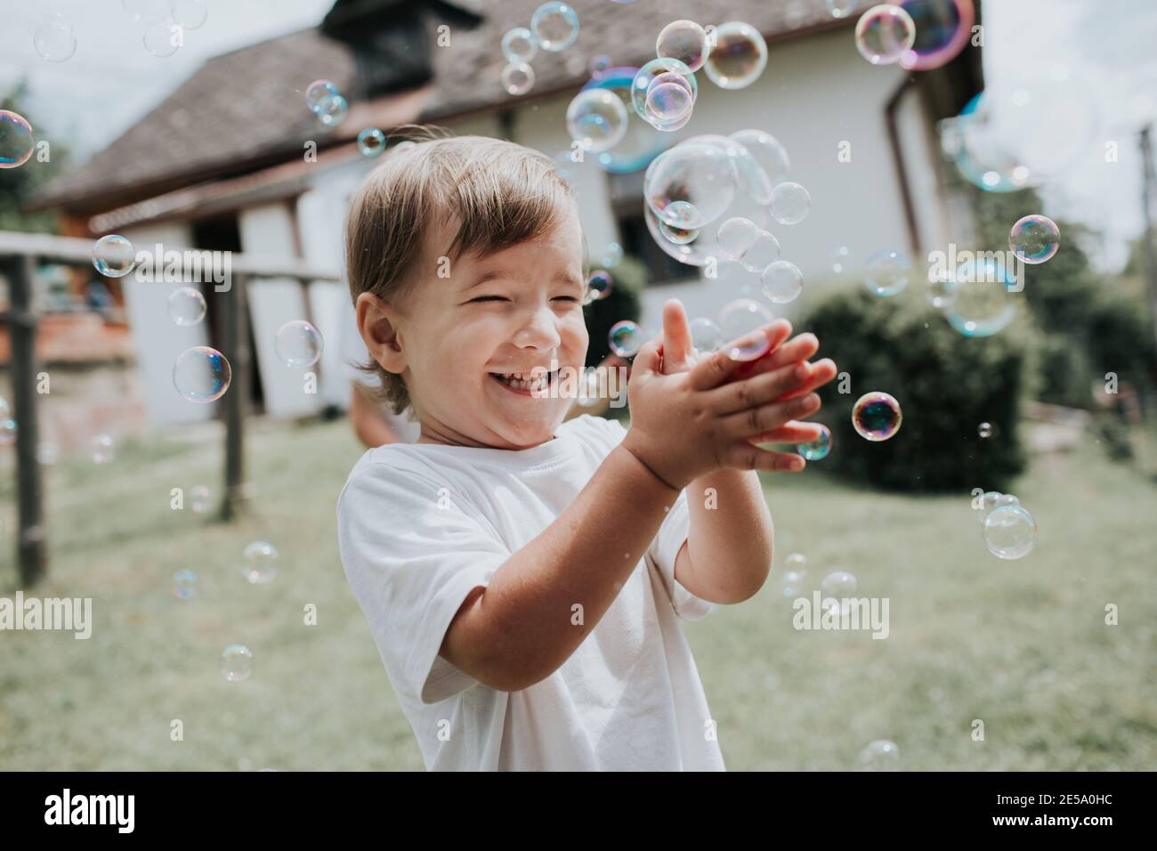 Bambino felice che schioccano le bolle del sapone. Il bimbo eccitato che fa scoppiare bolle di sapone in giardino in estate. Foto Stock