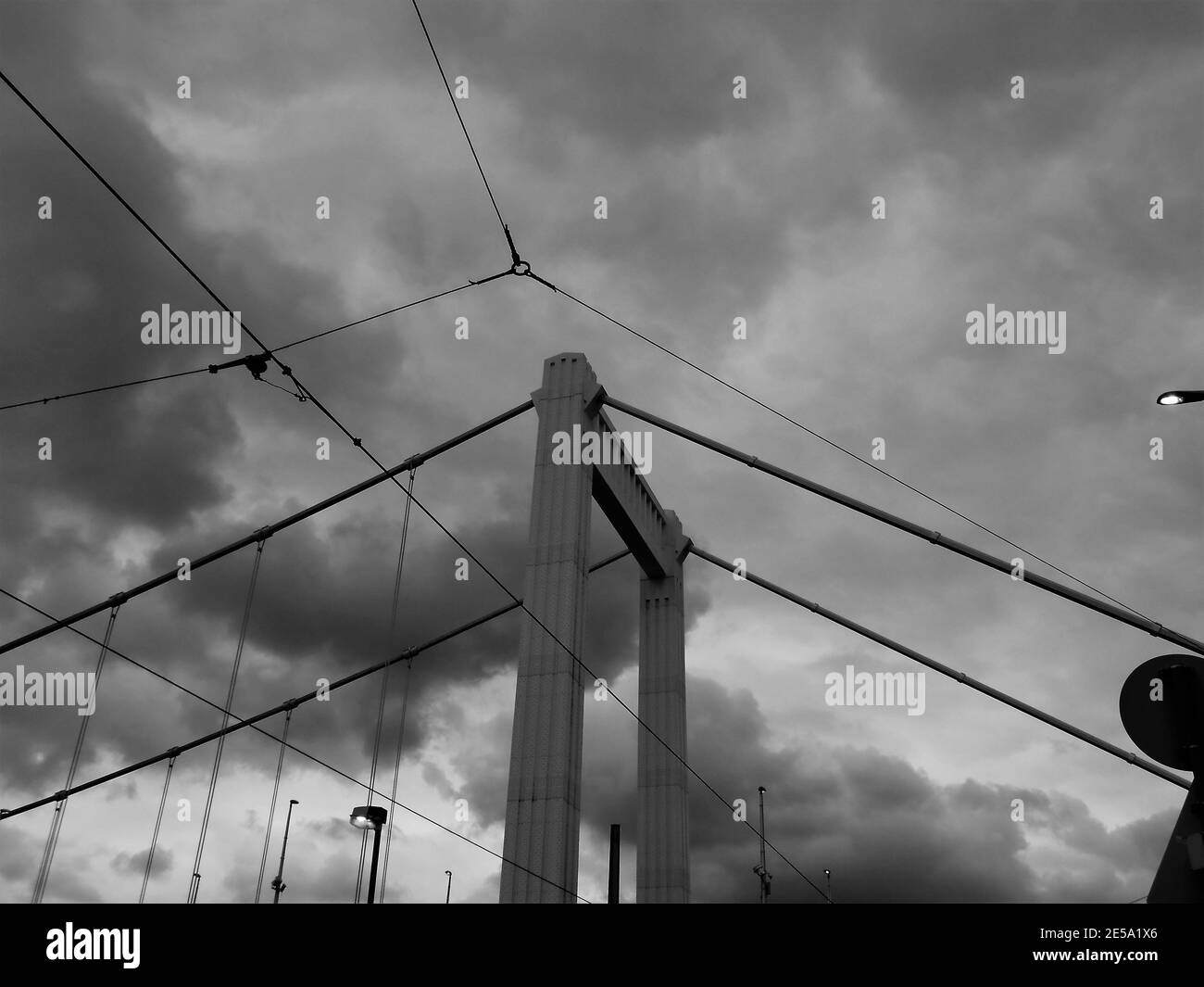 Immagine in scala di grigi delle linee elettriche e del ponte dei cavi con un Cielo nuvoloso su di esso a Budapest Foto Stock