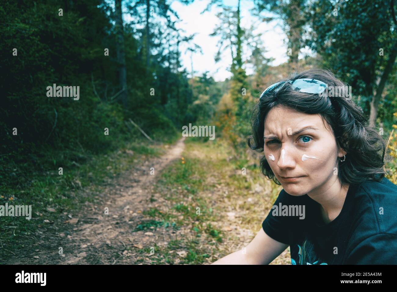 Ritratto di una ragazza dagli occhi blu che guarda la macchina fotografica e fa divertimento con crema solare sul viso in natura Foto Stock