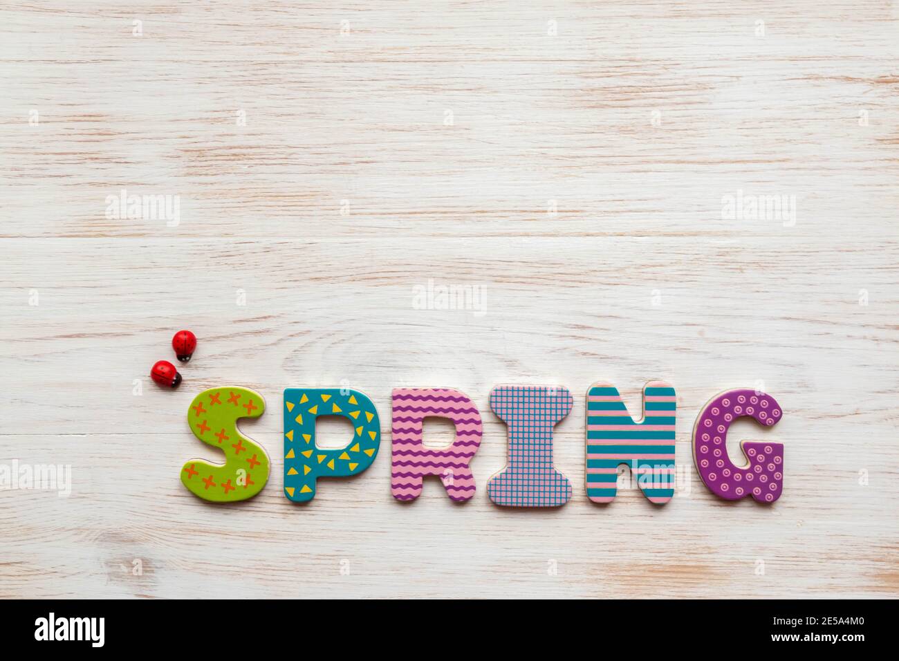 Iscrizione primavera scritta in colorate lettere di legno e due piccoli ladybirds di legno rosso su sfondo legno vintage. Sfondo primaverile con titolo Foto Stock