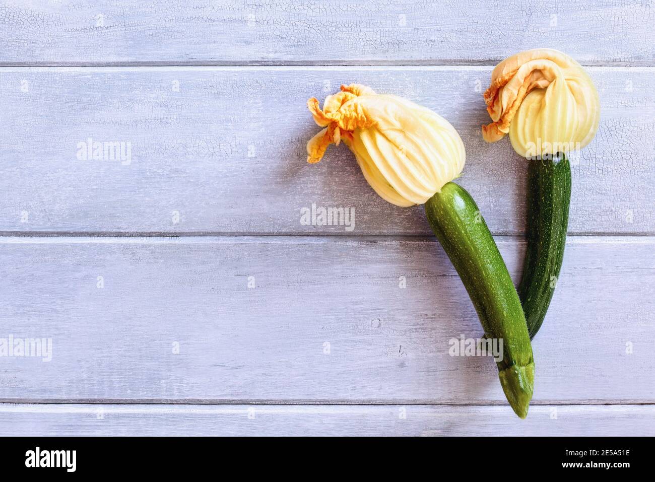 Flatlay di Courgette bambino o zucca zucchina con fiori su un rustico tavolo di legno blu. Ripresa dalla vista superiore con spazio per la copia. Foto Stock