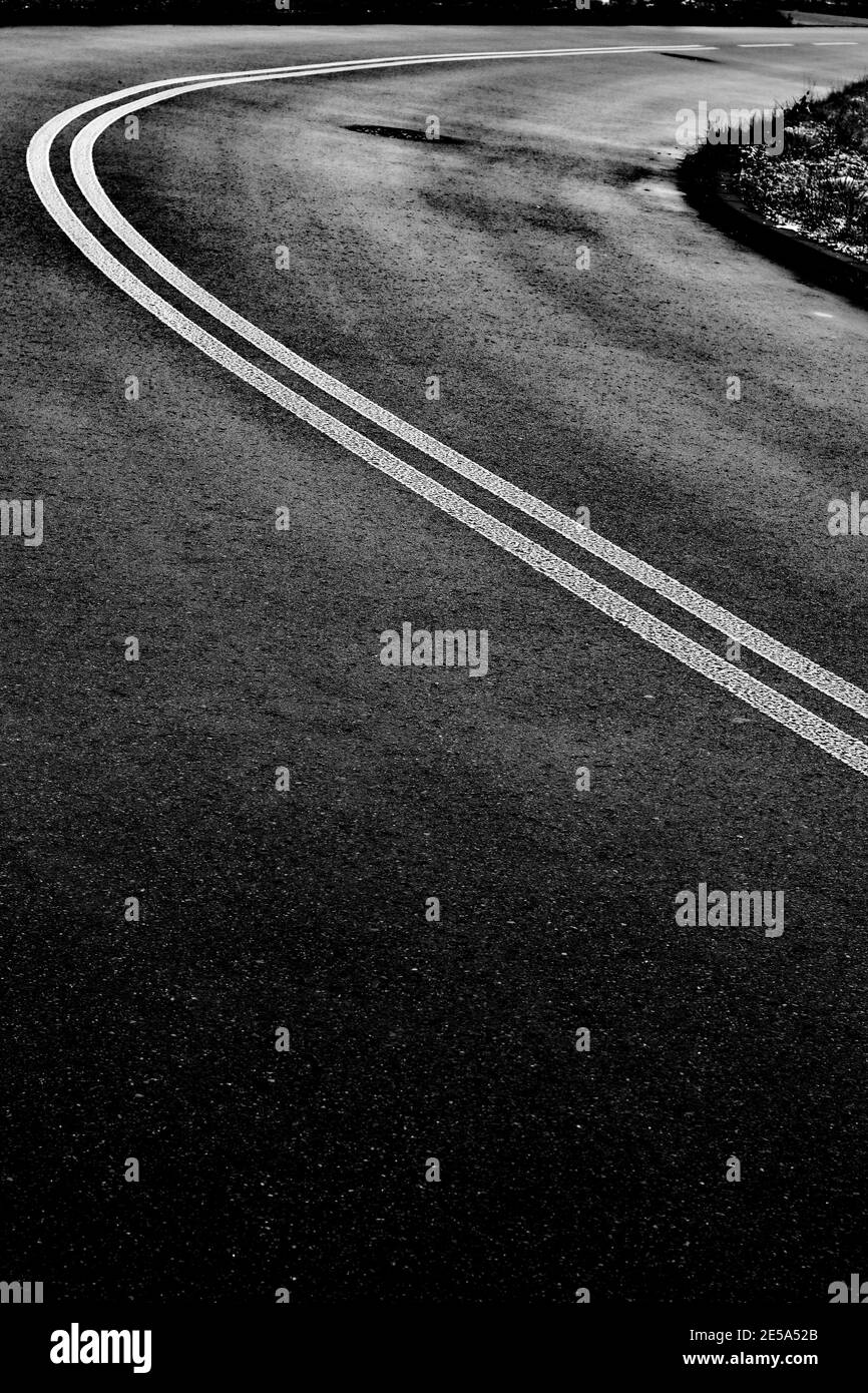 Curva stradale in asfalto nero con doppia linea continua bianca Foto Stock