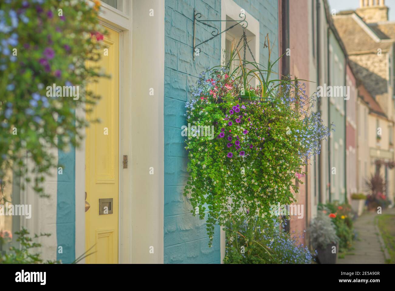 Bellissimi cestini Hanging Flower si aggirano all'esterno di colorate case dipinte Una strada in Scozia Foto Stock