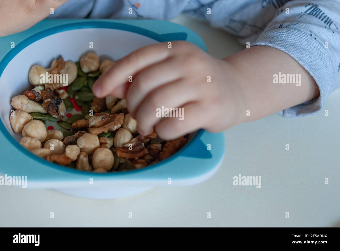 Il bimbo mangia con le mani noci grezze dal piatto dei bambini. Foto Stock