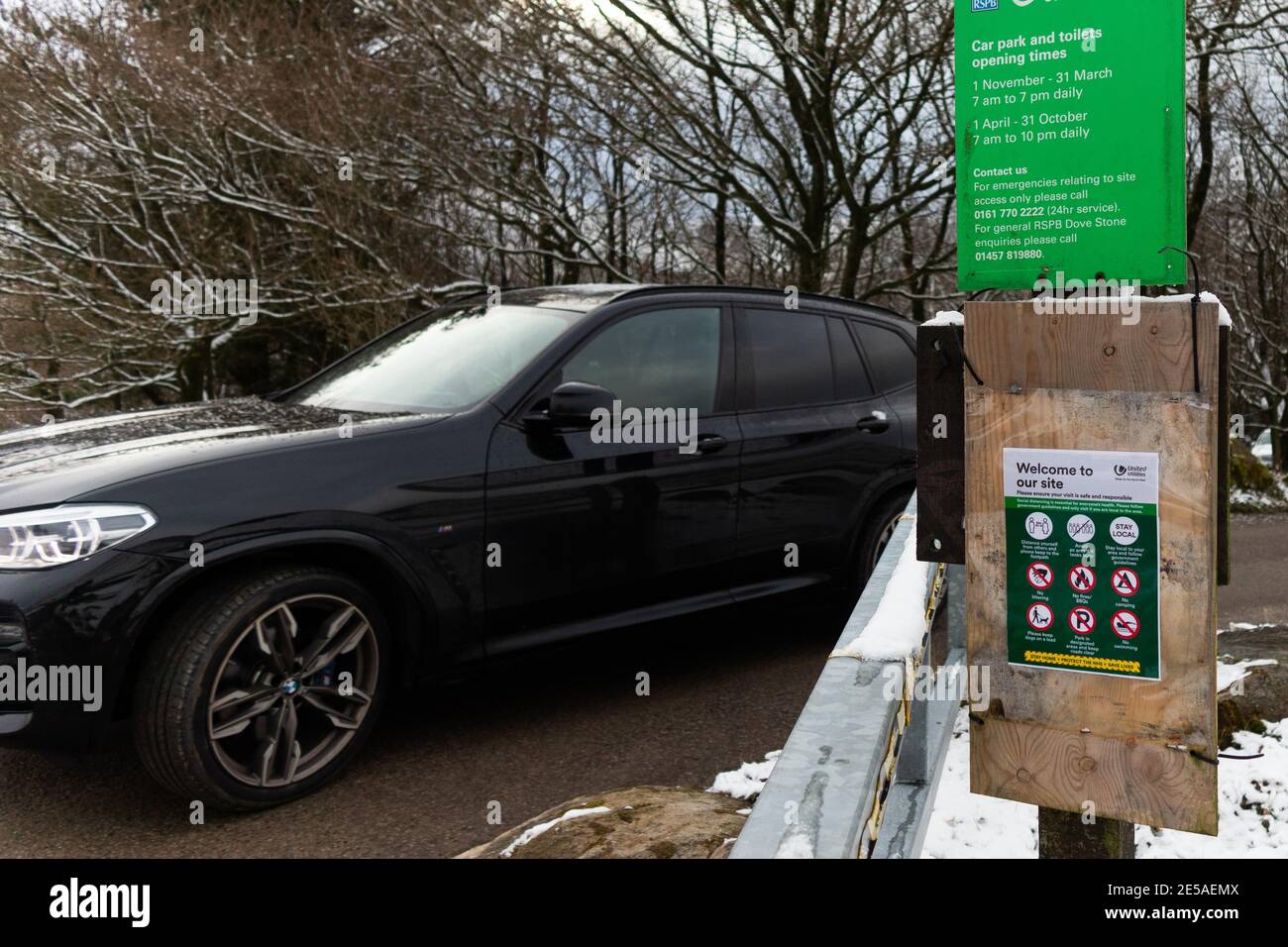 Un'auto per i visitatori passa davanti a un poster informativo di Covid mentre lascia il parcheggio Binn Green presso la Riserva Naturale di dove Stone, Saddleworth, Oldham Foto Stock